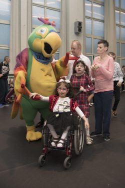 Zdjęcie grupowe. Duża maskotka papuga, chłopiec i trzy dziewczynki, jedna na wózku inwalidzkim.