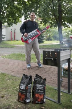 Mężczyzna z instrumentem muzycznym stoi przy grillu.