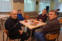 Czterech mężczyzn siedzi przy stoliku na którym stoją talerze ze słodyczami.