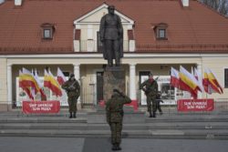 Trzej żołnierze stoją na baczność przed pomnikiem Józefa Piłsudskiego. Jeden z nich salutuje.