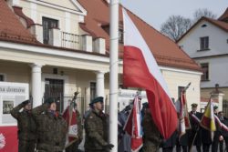 Biało czerwona flaga wciągana na maszt przez żołnierzy.