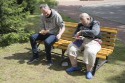 Dwaj mężczyźni siedzący na ławce jedzą kiełbasę.