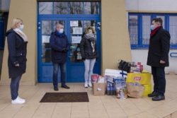 Dwie kobiety i dwóch mężczyzn stoją przed wejściem do budynku. Pomiędzy nimi na ziemi pudełak i torby z prezentami.