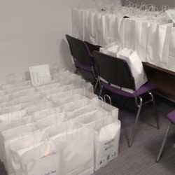 Białe torby z prezentami stojące na podłodze, stoliku i krzesłach.