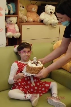 Uśmiechnięta dziewczynak siedzi na kanapie i trzyma podawany przez panią tort.