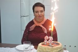 Uśmiechnięta kobieta. Przed nią na stole stoi tort ze świeczkami urodzinowymi.