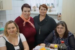 Cztery kobiety przy stoliku w pomieszczeniu z białymi kafelkami i szafkami.
