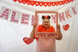 Kobieta na wysokości twarzy trzyma ramkę z napisem: free kiss! W tle za nią napis: Walentynki.