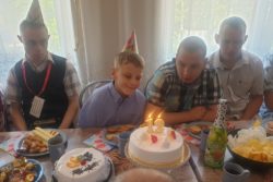 Czterej chłopcy siedzący przy stole zastawionym słodyczami i stojącym tortem.