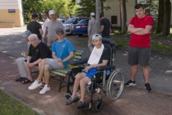 Mężczyźni siedzący na ławce i stojący obok ławki. Jeden z nich siedzi na wózku inwalidzkim.