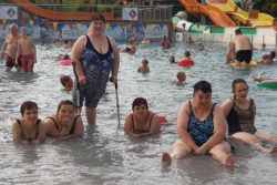 Sześć kobiet w strojach kąpielowych na dużym basenie. W tle kąpiące się inne osoby.