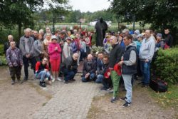 Zdjęcie grupowe. Kobiety i mężczyźni stojący przy pomniku Jana Pawła II.