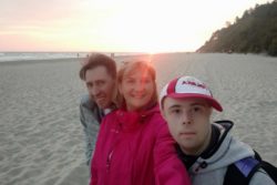 Kobieta i dwóch mężczyzn na plaży na tle wschodzącego słońca.