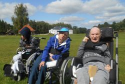 Trzech mężczyzn na wózkach inwalidzkich na tle zieleni.
