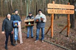 Czterej mężczyźni trzymający otrzymane karmniki dla ptaków. W tle las.