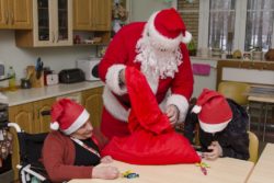 Mikołaj rozdający słodycze osobom siedzącym przy stoliku.