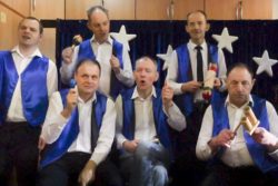 Sześciu mężczyzn w białych koszulach i niebieskich kamizelkach z instrumentami muzycznymi w rękach.