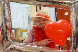 Kobieta w słomkowym kapeluszu trzymająca czerwony balonik w kształcie serca.