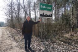 Mężczyzna stojący przy tablicy z nazwą miejscowości Bobrowa.