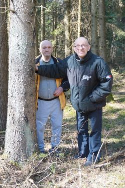 Dwaj mężczyźni stojący obok drzewa w lesie.