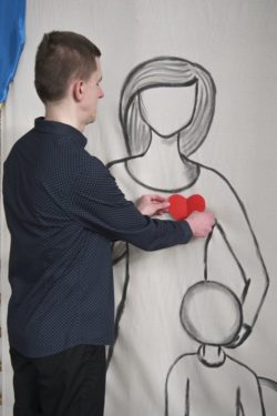 Mężczyzna przyczepiający czerwone serce do postaci namalowanej na płutnie.