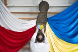 Mężczyzna przyczepiający niebiesko-żółte srce do dekoracji w barwach polskich i ukraińskich.