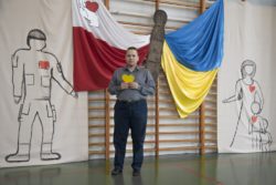 Mężczyzna trzymający w dłoniach żółte serce na tle dekoracji w barwach Polski i Ukrainy.