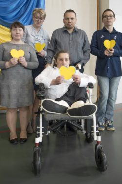 Pięć osób trzymających w dłoniach żółte serca.