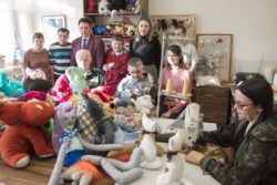 Zdjęcie grupowe. Kobiety i mężczyźni siedzący i stojący za stołem na którym leży dużo pluszowych zabawek.