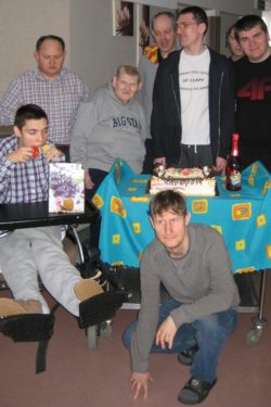 Siedmiu mężczyzn atojących wokół stołu na którym stoi tort i butelka szampana.