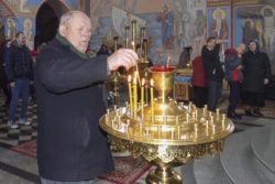 Grupa osób w cerkwi. Jeden z mężczyzn wstawia świeczkę do świecznika.
