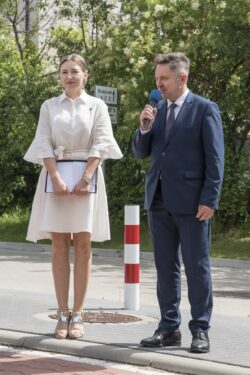 Kobieta i mężczyzna stojący na chodniku. Mężczyzna trzyma w ręku mikrofon.