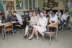 Grupa osób siedząca na krzesłach w sali szkolnej. Na pierwszym planie dwie siedzące kobiety.
