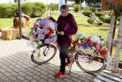 Kobieta stojąca przy rowerze przyozdobionym kwiatami.
