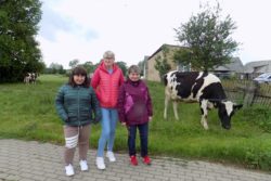 Trzy kobiety stojące na tle łąki i pasącej się na niej krowy.