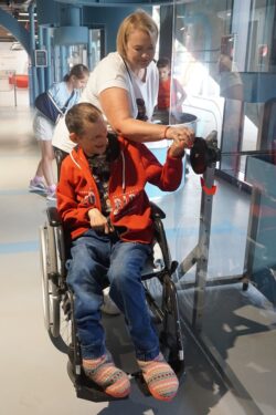 Kobieta i mężczyzna na wózku inwalidzkim wewnątrz pomieszczenia przy ekspozycji.