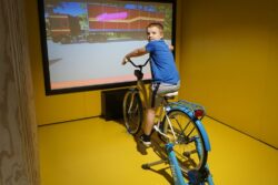 Chłopiec siedzący na rowerze przed dużym ekranem.