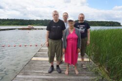 Kobieta i czterech mężczyn stojący na pomoście nad jeziorem.