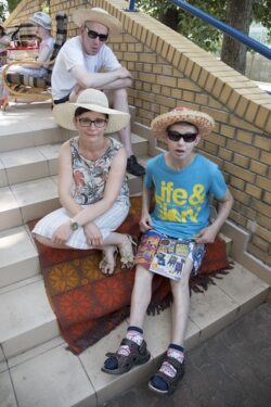 Kobieta i dwóch mężczyzn w letnich kapeluszach siedzący na rozłożonym na schodach kocu.