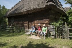 Trzy kobiety siedzące na ławce przed drewnianą chatą.