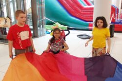 Troje dzieci stojące przy kolorowej chuście.