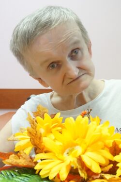 Siedząca przy stole kobieta trzyma w dłoniach kolorowe kwiaty.