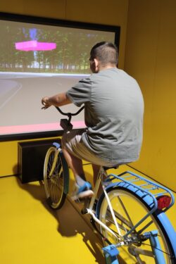 Chłopiec jadący rowerem stacjonarnym przed dużym ekranem.