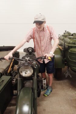 Chłopiec stojący przy motocyklu wojskowym.