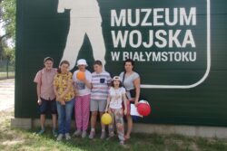 Sześć osób stojących przed planszą z napisem Muzeum Wojska w Białymstoku.