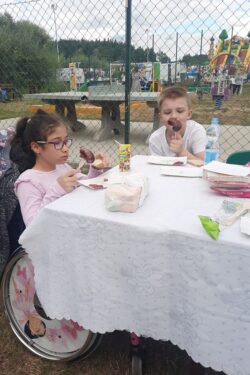 Dziewczynka i chłopiec siedzący przy stole i jedzący smarzoną kiełbasę.