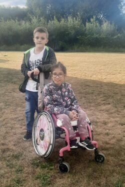 Chłopiec stojący przy dziewczynce siedzącej na wózku inwalidzkim.