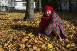 Kobieta przykucająca na trawniku pokrytym żółtymi liśćmi.