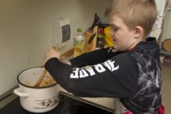 Chłopiec mieszający zawartość garnka stojącego na kuchence.