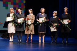 Sześć kobiet stojących na scenie. Każda z kobiet trzyma w rękach kwiat i dyplom.